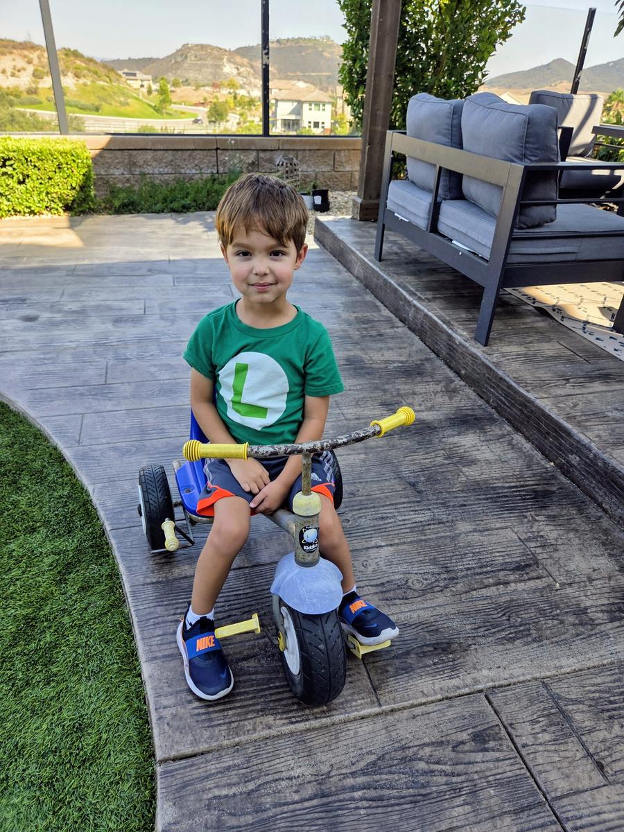 A boy sitting on a trike on the patio, with the hills of Harmony Grove behind him.